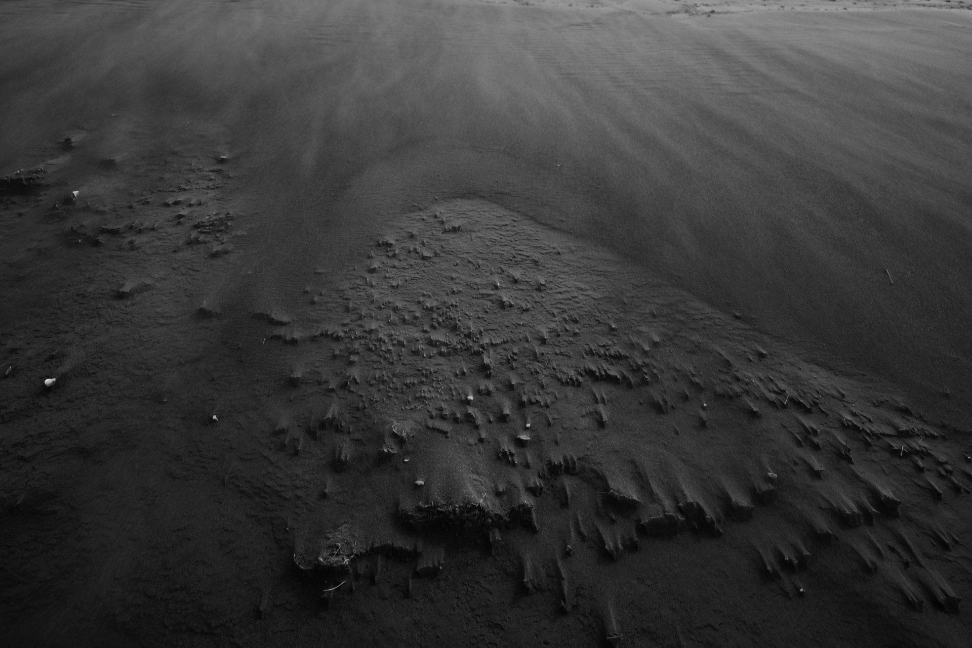 A black and white photo of a rock in the sand on a beach.